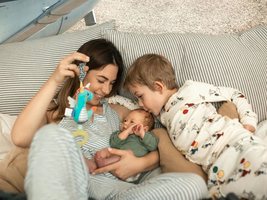 Eine Mutter kuschelt mit ihrem Kleinkind und Baby auf dem Sofa.