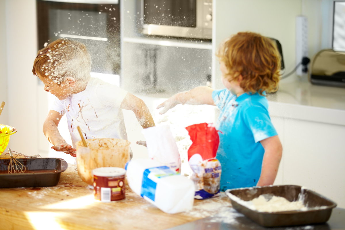 Zwei Kinder streiten beim Backen und bewerfen sich mit Mehl.