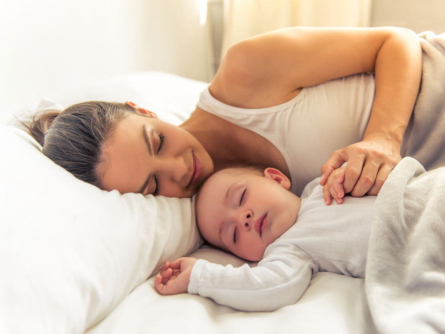 Baby und Mutter schlafen zusammen im Bett.