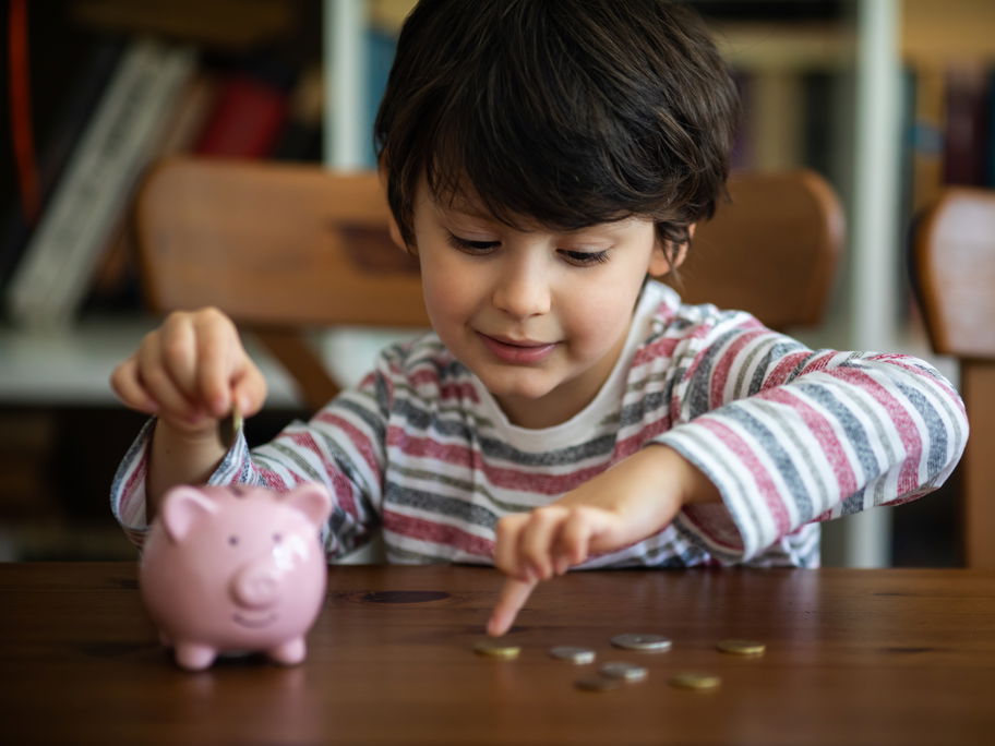 Junge steckt Geld in sein Sparschwein.
