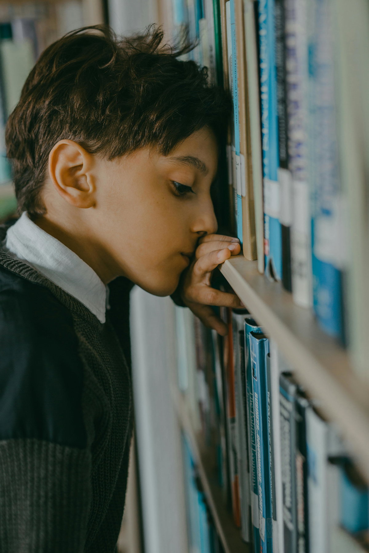 Nachdenklicher Junge lehnt Kopf gegen Bücherregal.