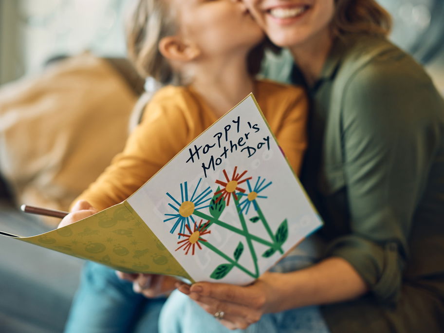 Kind küsst Mutter und schenkt ihr eine Karte zum Muttertag.