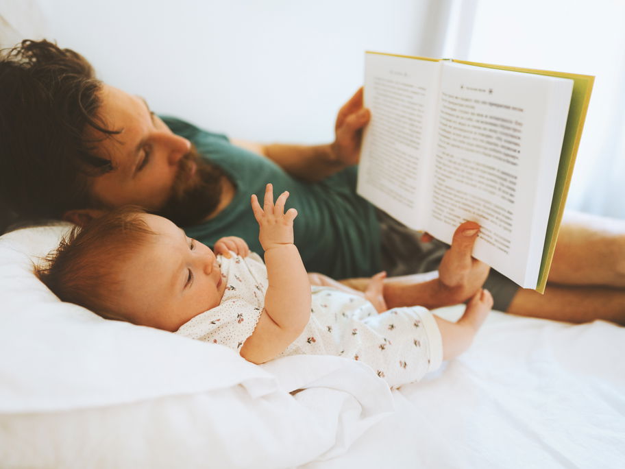 Vater liest Baby im Bett vor.
