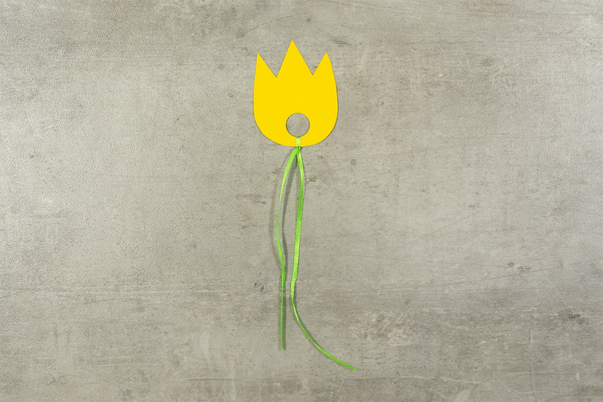 Fertig ist eure erste Papier-Tulpe. Das geschwungene grüne Satinband sieht aus wie der Stil und wirkt edel. Auf diese Art könnt ihr beliebig viele verschiedenfarbige Frühlingstulpen aus Papier herstellen und aufhängen.