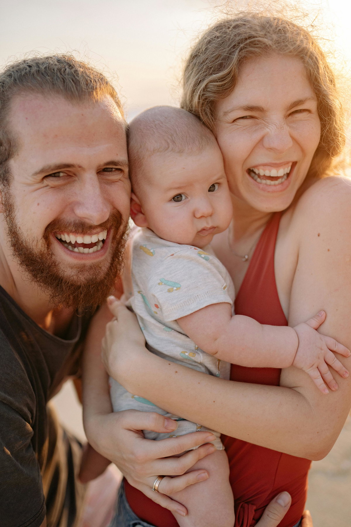 Eltern lachen mit Baby auf dem Arm.