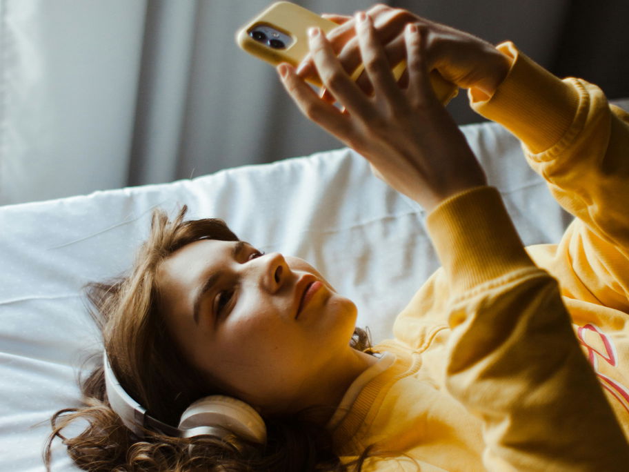 Frau im Bett am Handy mit Kopfhörern.