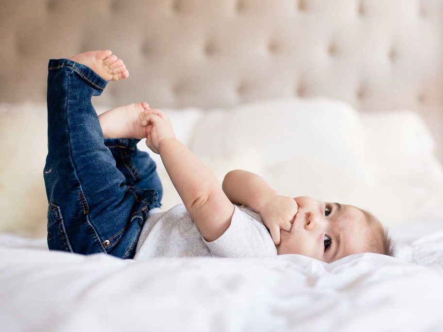 Ein kleines Baby mit Jeans liegt auf einem Bett.