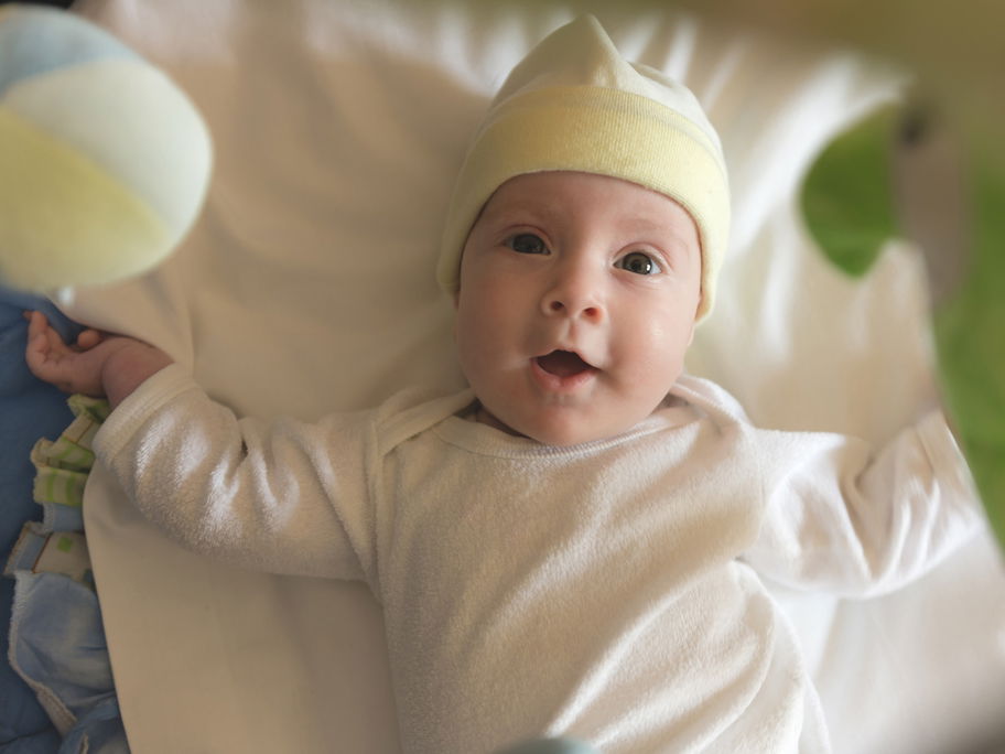 Baby liegt fröhlich unter einem Mobile.