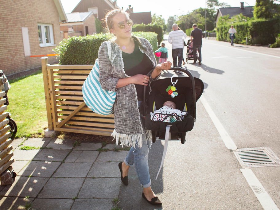 Eine Mutter trägt ihr Baby im Maxi Cosi über die Straße