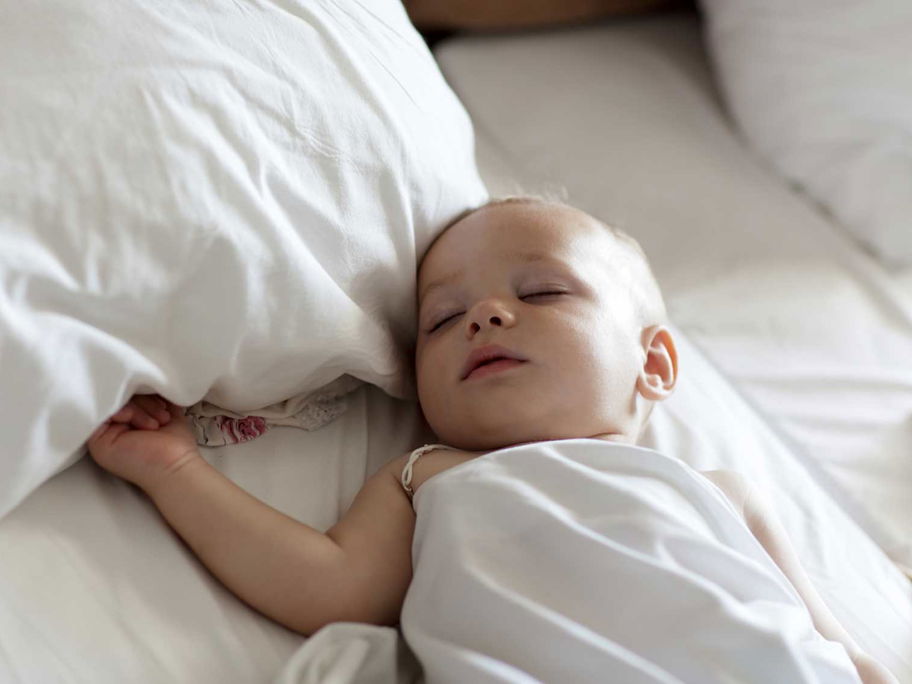 Baby schläft in einem Bett mit großen Kissen.