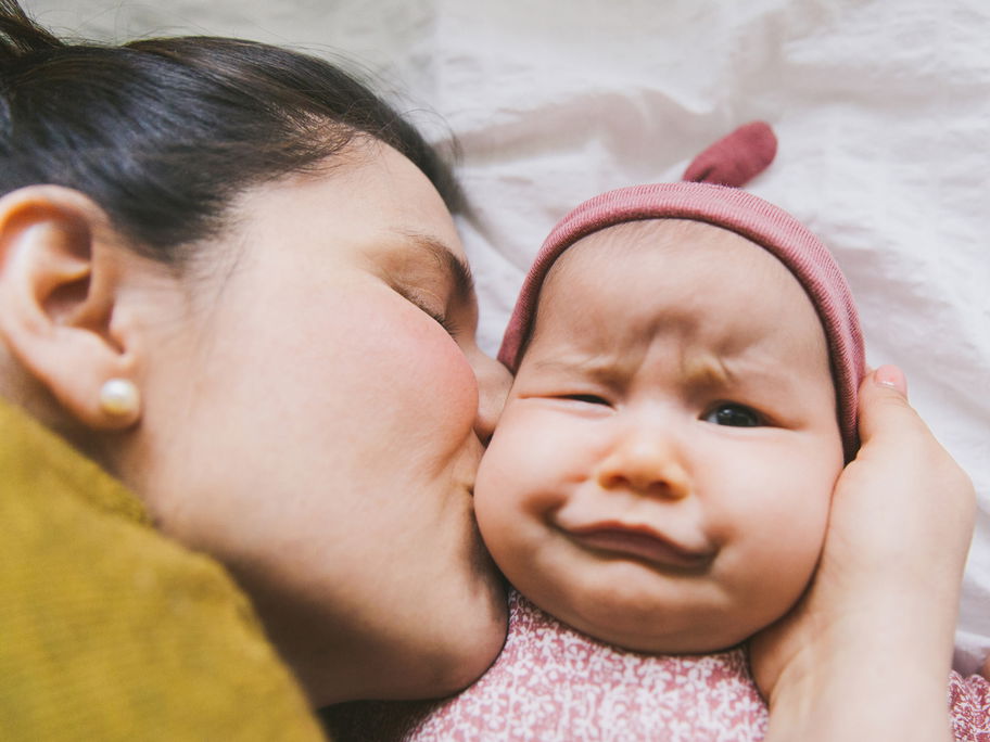 Ein Baby wird von seiner Mama geküsst und verdreht dabei die Augen.