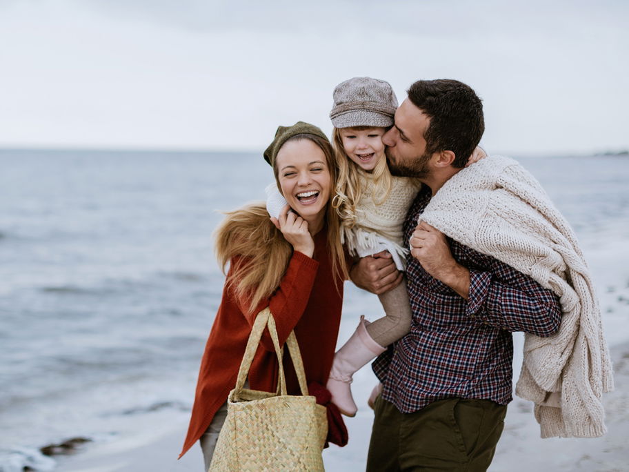 Mutter, Vater und Kind gehen am Strand spazieren.