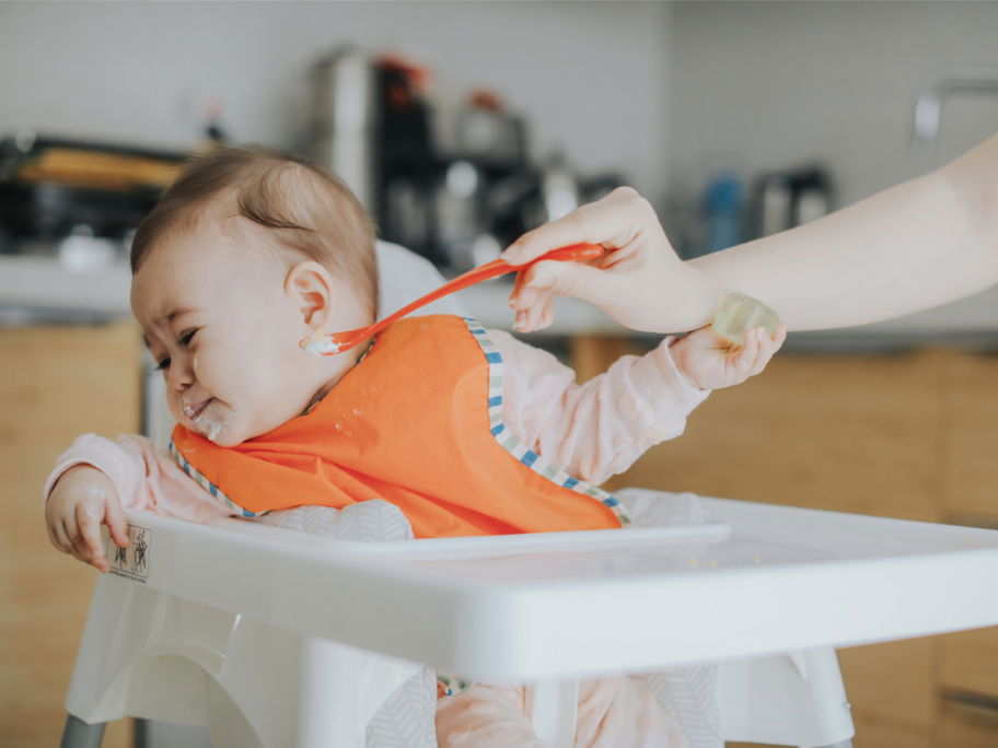 Ein Baby, das mit Brei gefüttert werden soll, dreht seinen Kopf weg.