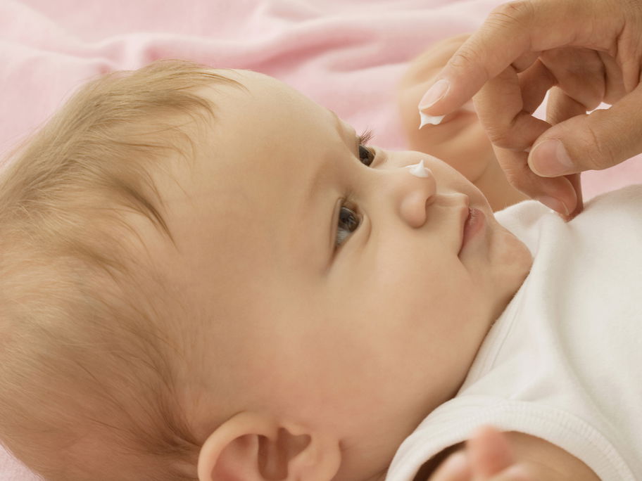 Baby bekommt Creme auf die Nase getupft.
