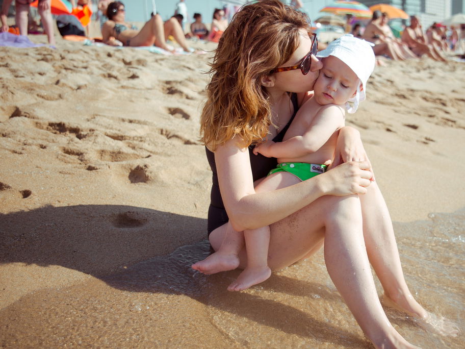 Eine Mama und ihr Baby kuscheln am Strand.