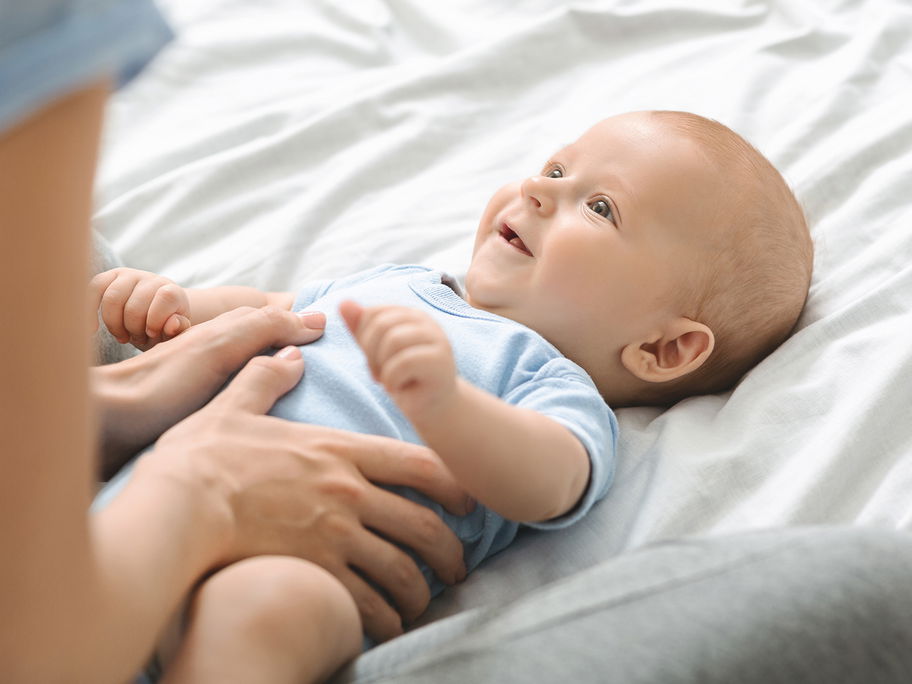 Mama hält Bäuchlein eines fröhlichen Babys.
