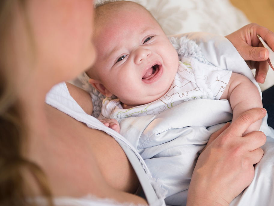 Eine Mutter misst bei ihrem weinenden Baby mit einem Fieberthermometer die Temperatur.