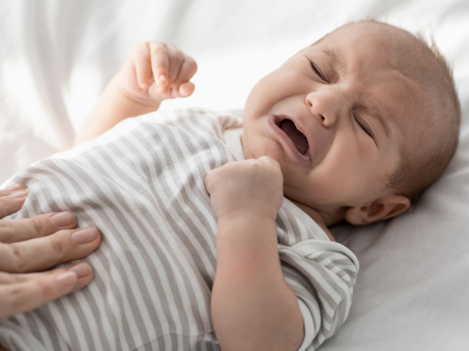Weinendes Baby, dessen Bäuchlein massiert wird.