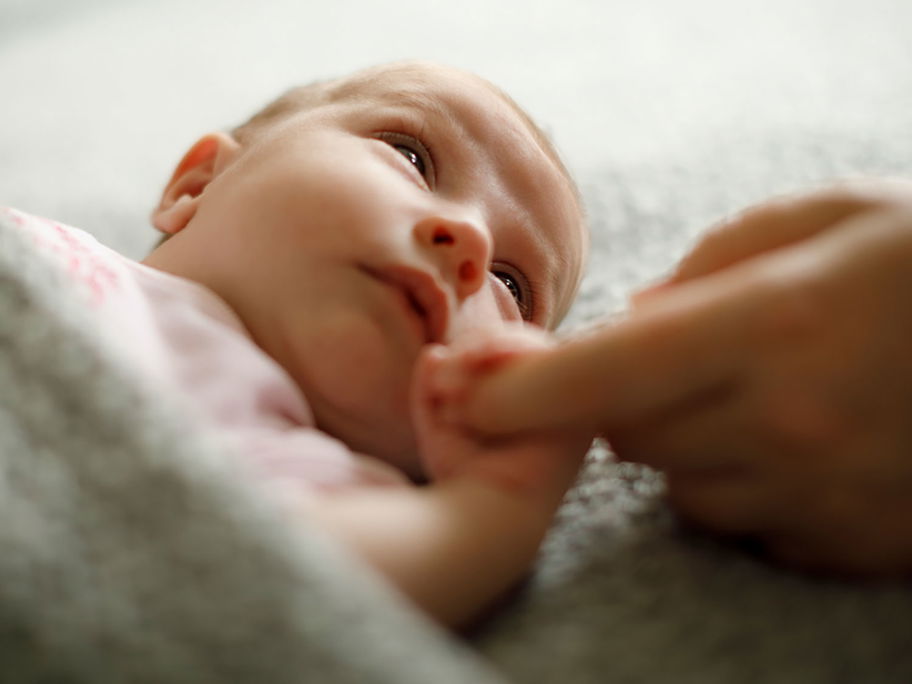 Müdes Baby hält Finger eines Elternteils.