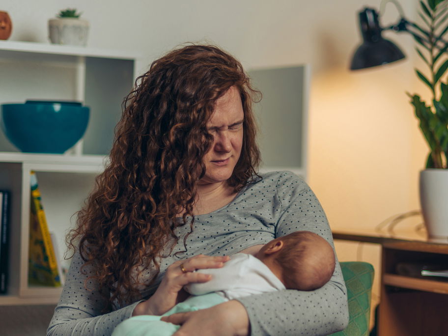 Frau stillt mit schmerzverzerrtem Gesicht ihr Baby.