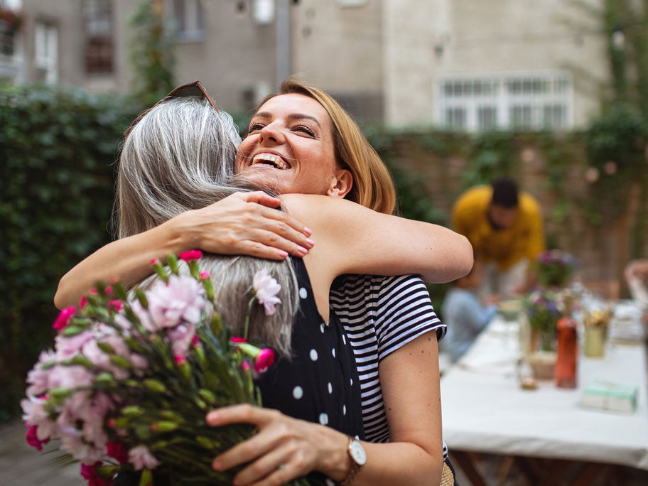 Erwachsene Frau umarmt ihre Mutter mit Blumen.