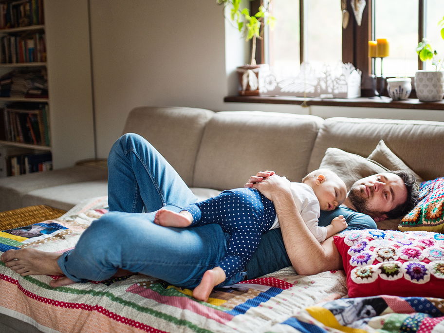 Baby und Papa liegen schlafend auf dem Sofa.