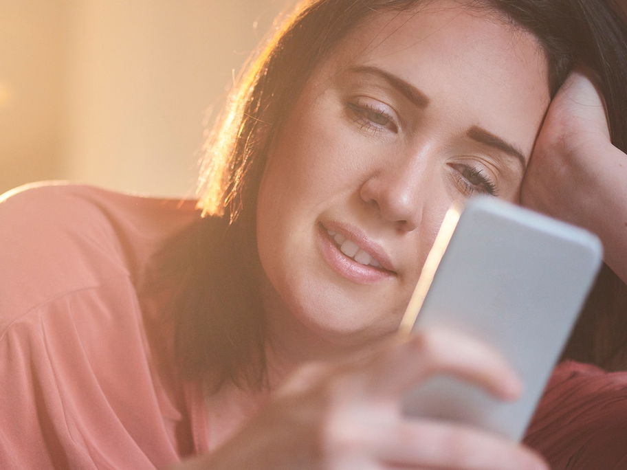 Frau lächelt, während sie auf ihr Smartphone schaut.