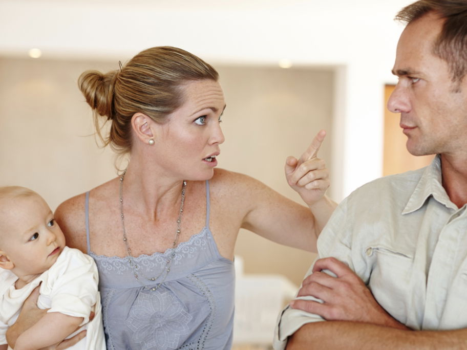 Mutter mit Baby auf dem Arm spricht belehrend mit ihrem Mann.