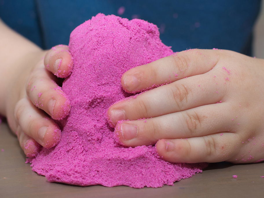 Kinderhände mit pinkfarbenem Kinetic Sand.
