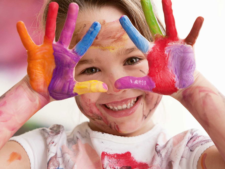 Fröhliches Kind mit bunten Fingerfarben an den Händen.