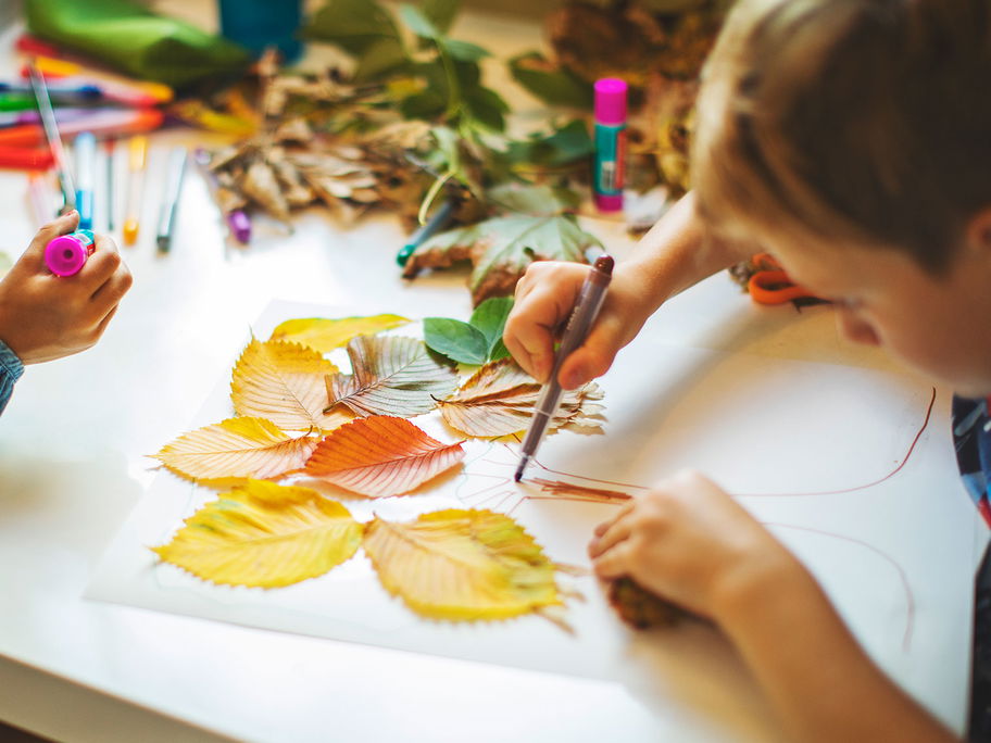 Kinder basteln mit Herbstblättern und Stiften.
