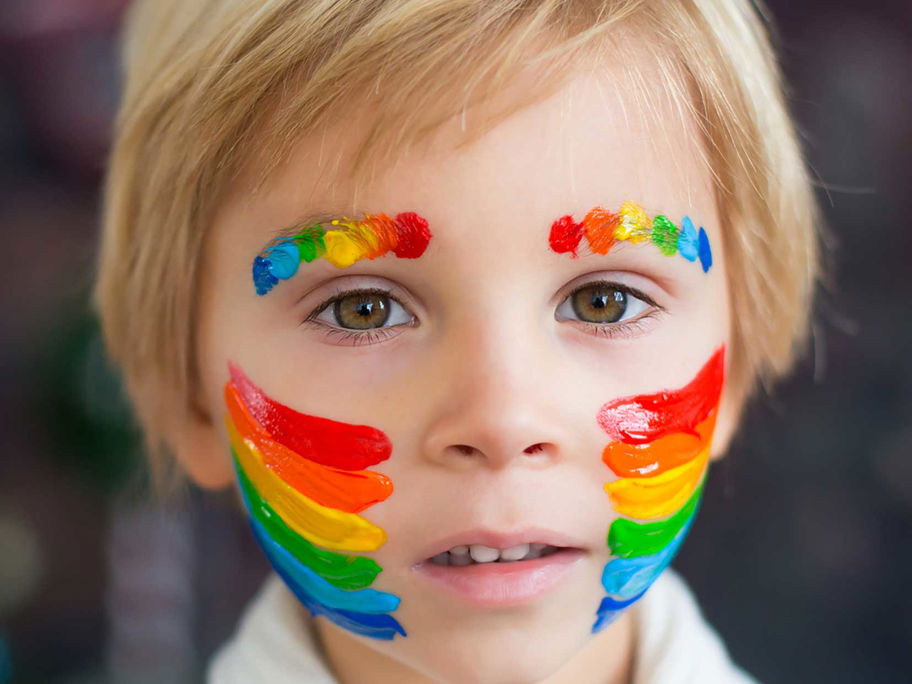 Junge mit geschminktem Regenbogen auf Wangen und Augenbrauen