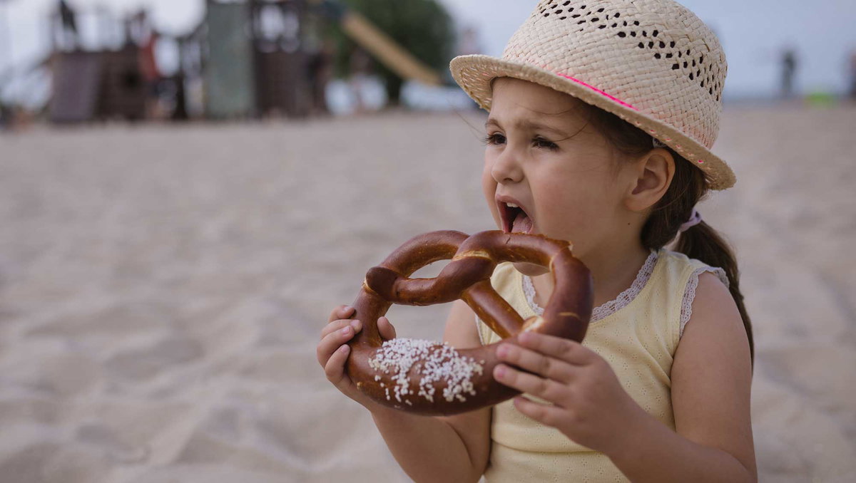 Mädchen beißt in eine Laugenbrezel mit viel Salz.