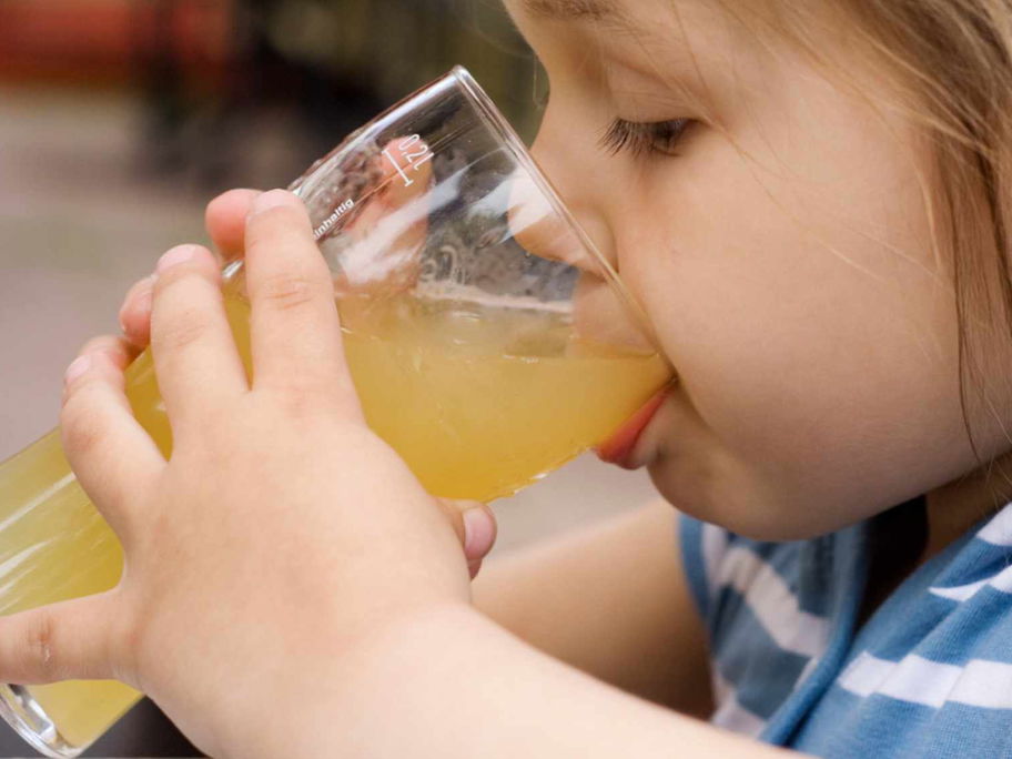 Kind trinkt Apfelsaft aus einem Glas.