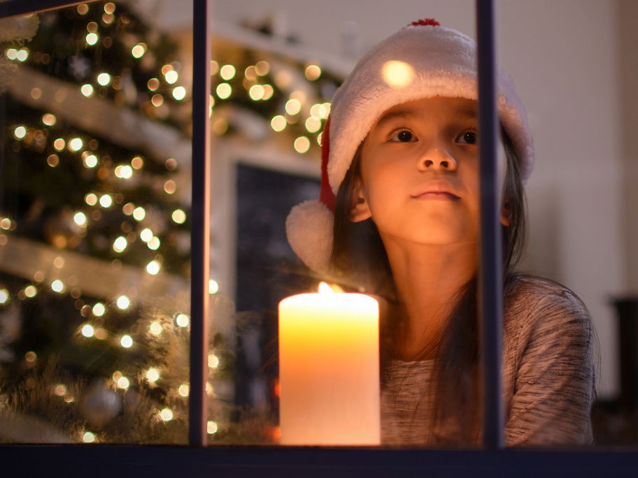 Ein Mädchen schaut aus einem weihnachtlichen Fenster.
