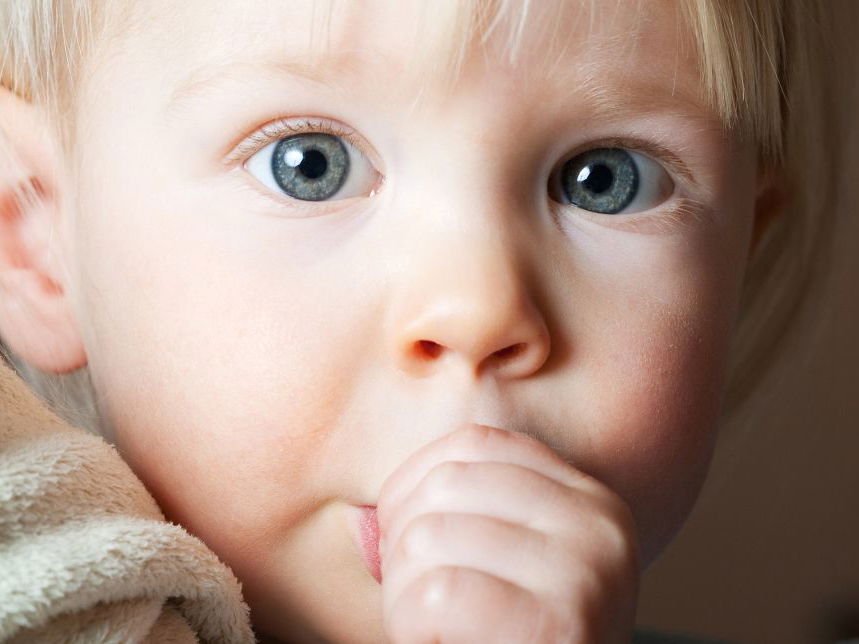 Kleines Kind nuckelt mit großen Augen am Daumen.