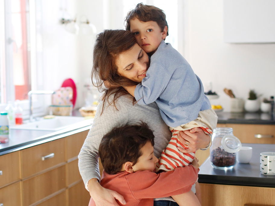 Mutter kuschelt in der Küche mit ihren beiden Kindern.