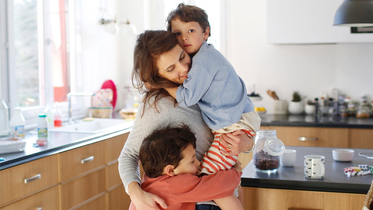 Mutter kuschelt in der Küche mit ihren beiden Kindern.