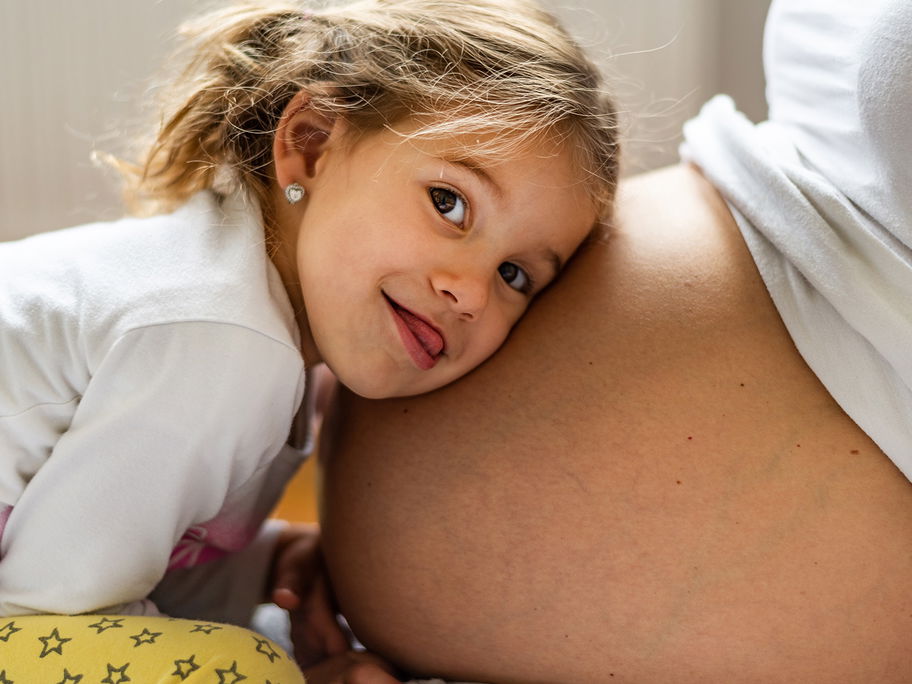 Fröhliches Mädchen lauscht am Babybauch.