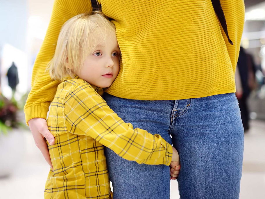 Kind umarmt das Bein seiner Mama, um ganz nah bei ihr zu sein