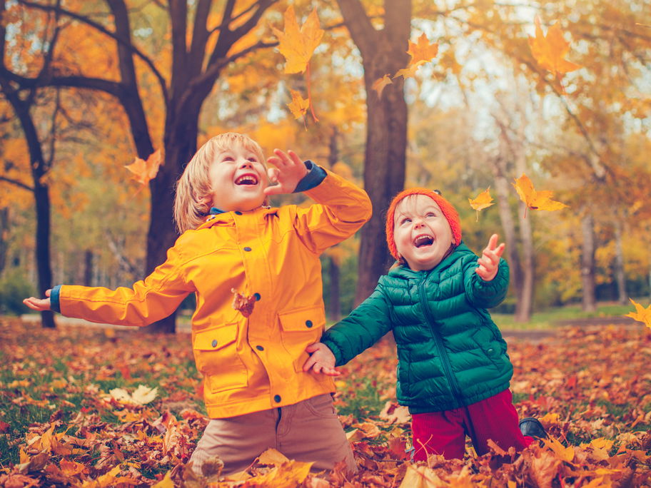 Zwei Kinder freuen sich über buntes Herbstlaub.