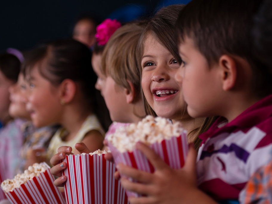 Zwei Kinder sitzen im Kino mit einer Tüte Popcorn in der Hand.
