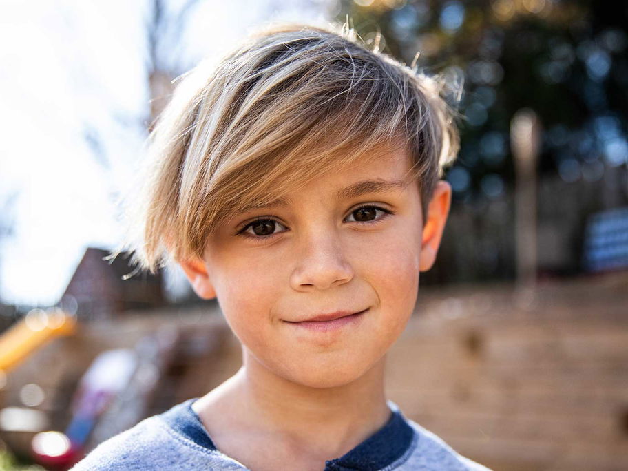Blonder Junge mit längeren Haaren lächelt.
