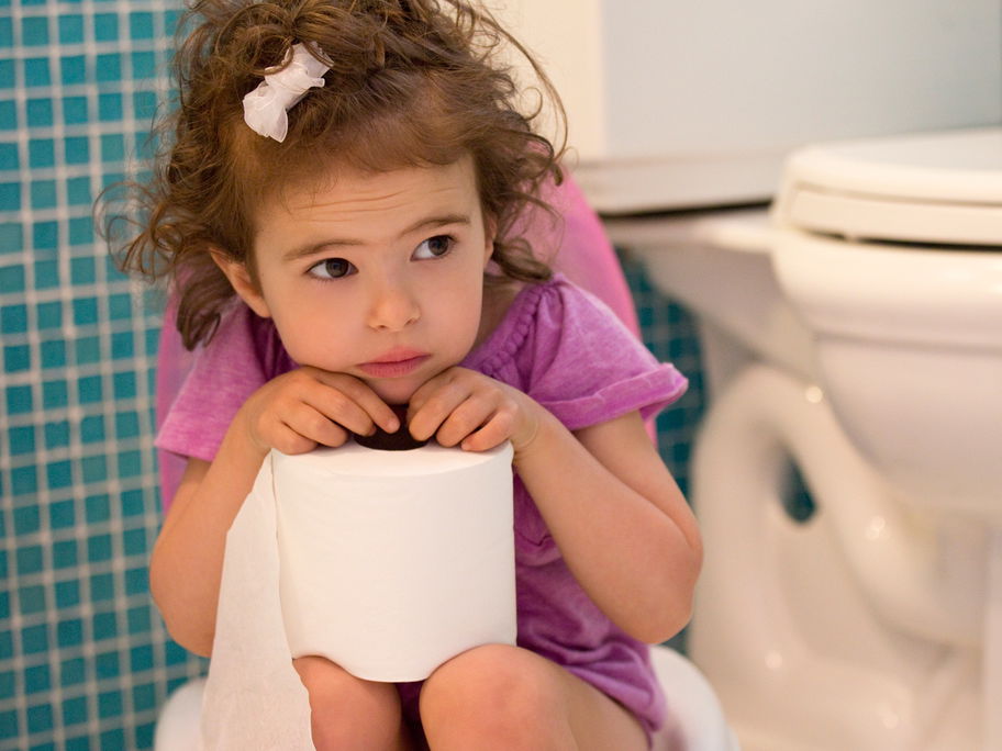 Ein kleines Mädchen sitzt auf der Toilette und schaut unglücklich.
