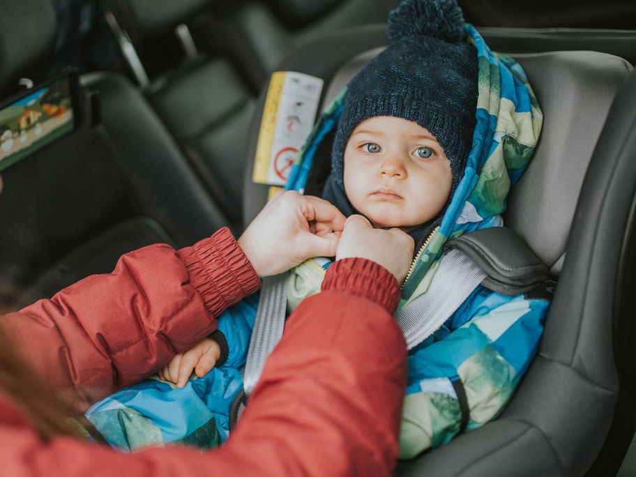 Frau schnallt Baby im Autokindersitz an.