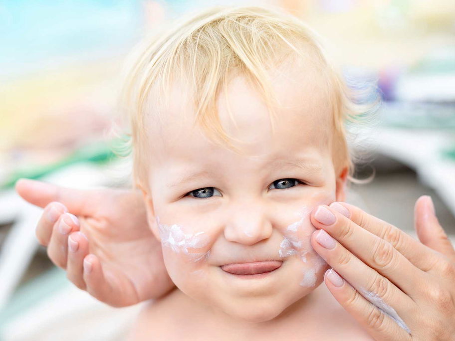 Baby wird mit Sonnencreme eingeschmiert.