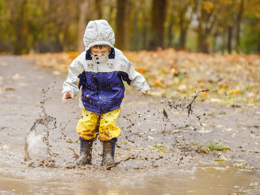 Ein kleiner Junge springt mit seiner Regenhose in einer Pfütze herum.
