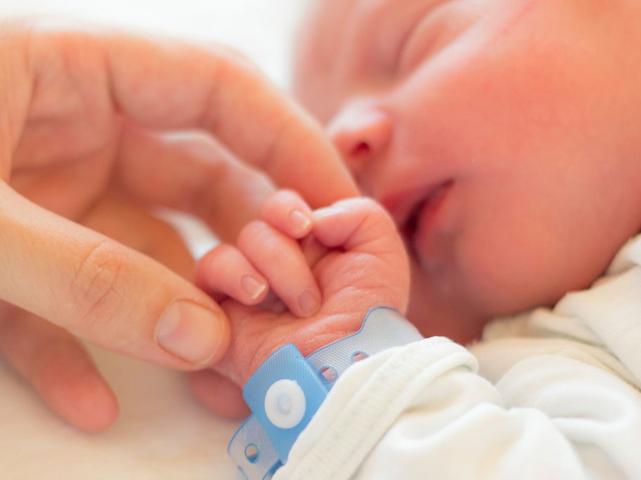 Eine Mama streichelt die Hand ihres neugeborenen Babys