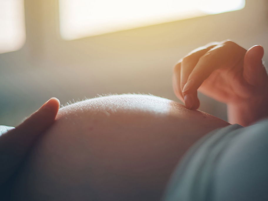 Schwangere berührt ihren Bauch mit Händen.