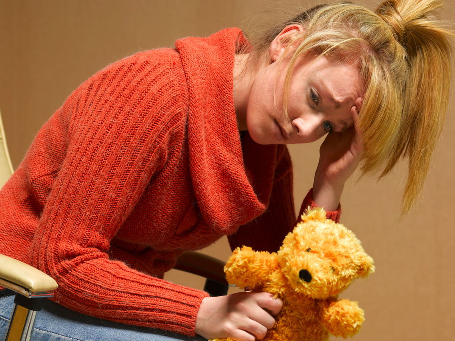 Erschöpfte, mutlose Frau mit Teddy in der Hand.